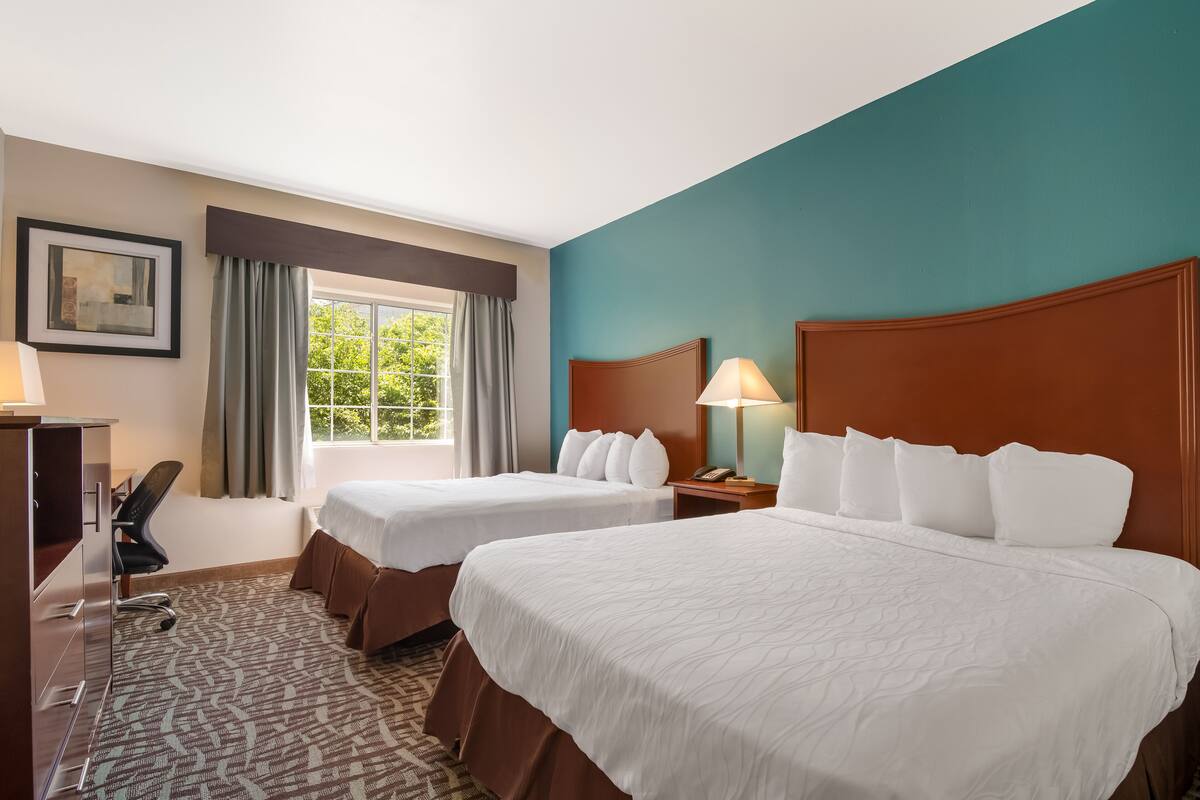 Habitación de hotel con dos camas, un escritorio, una silla y una ventana con cortinas.