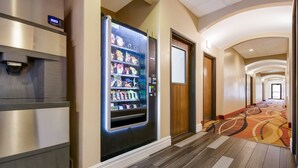 A hallway with a vending machine, a wooden door, and a carpeted floor. - SureStay Plus Hotel by Best Western Topeka Northwest (Topeka)
