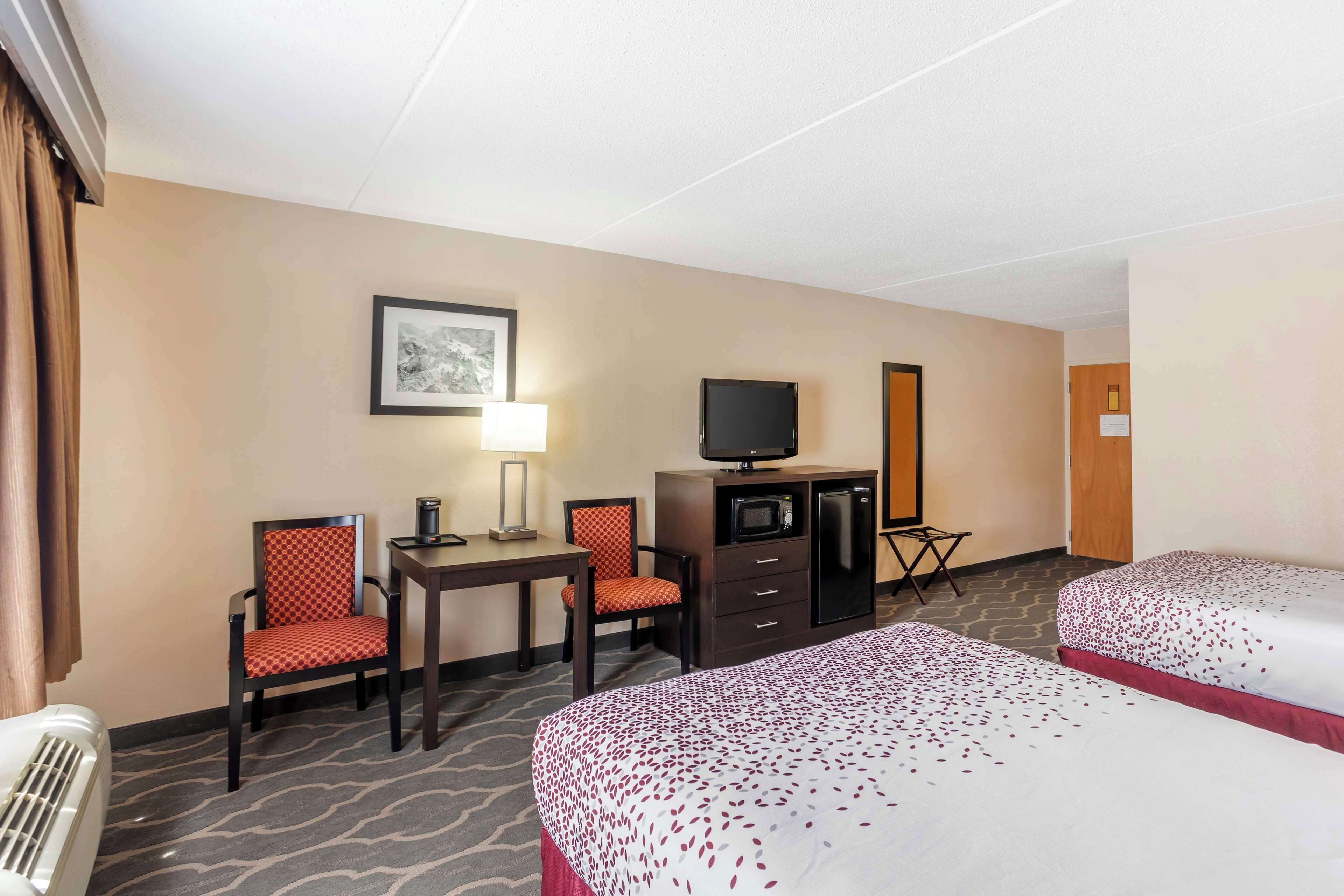 A hotel room with two beds, a desk with a chair, a television, and a microwave.