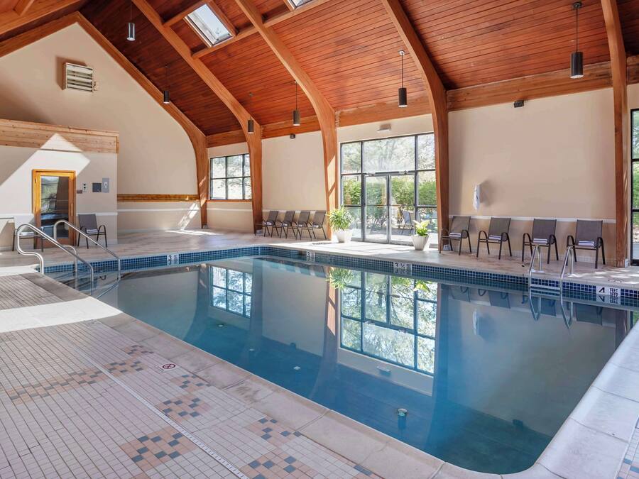 Una piscina interna con pavimento piastrellato, travi in legno a soffitto e ampie finestre.