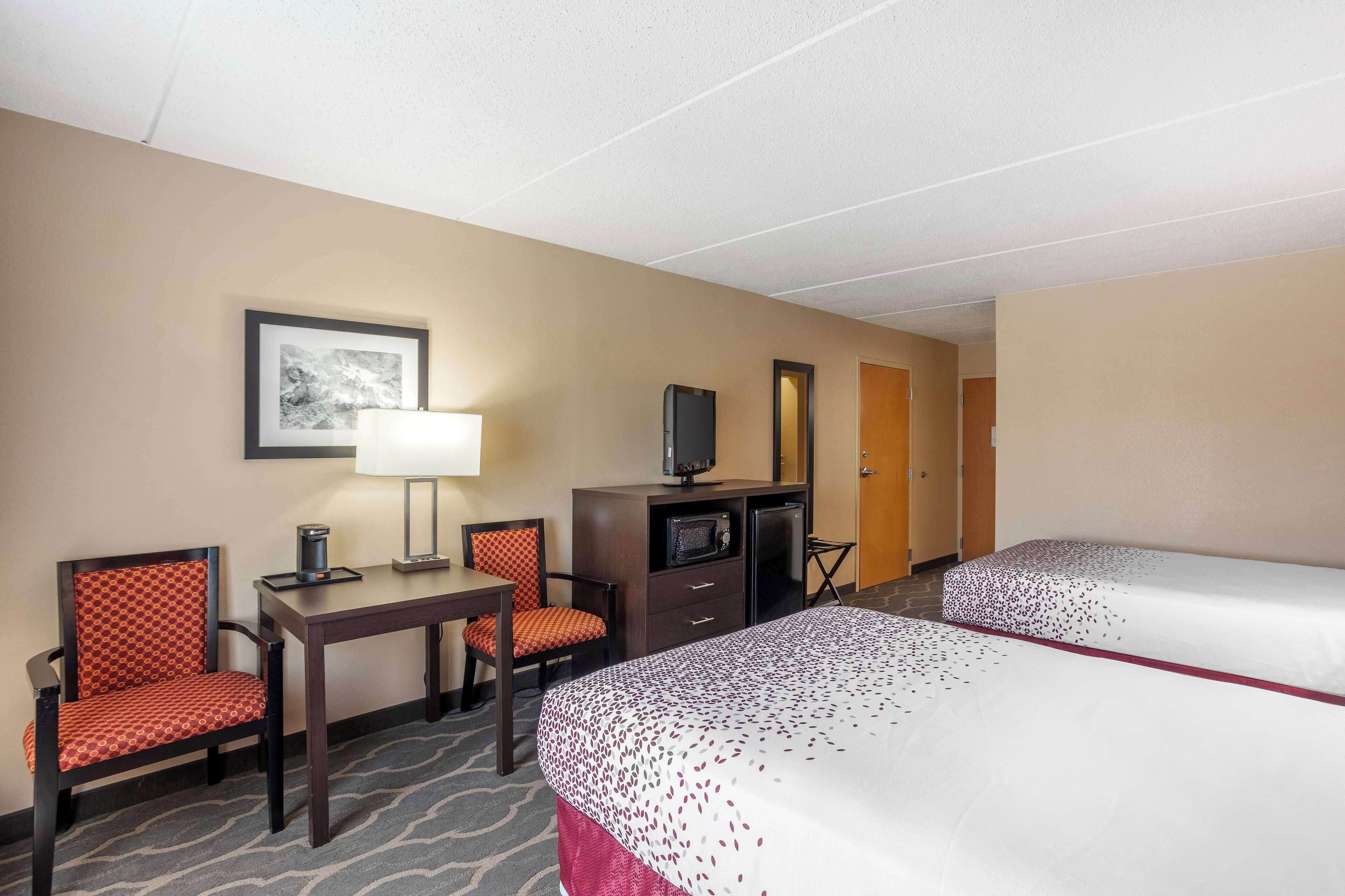 A hotel room with two beds, a desk with a lamp, a TV, and a chair.