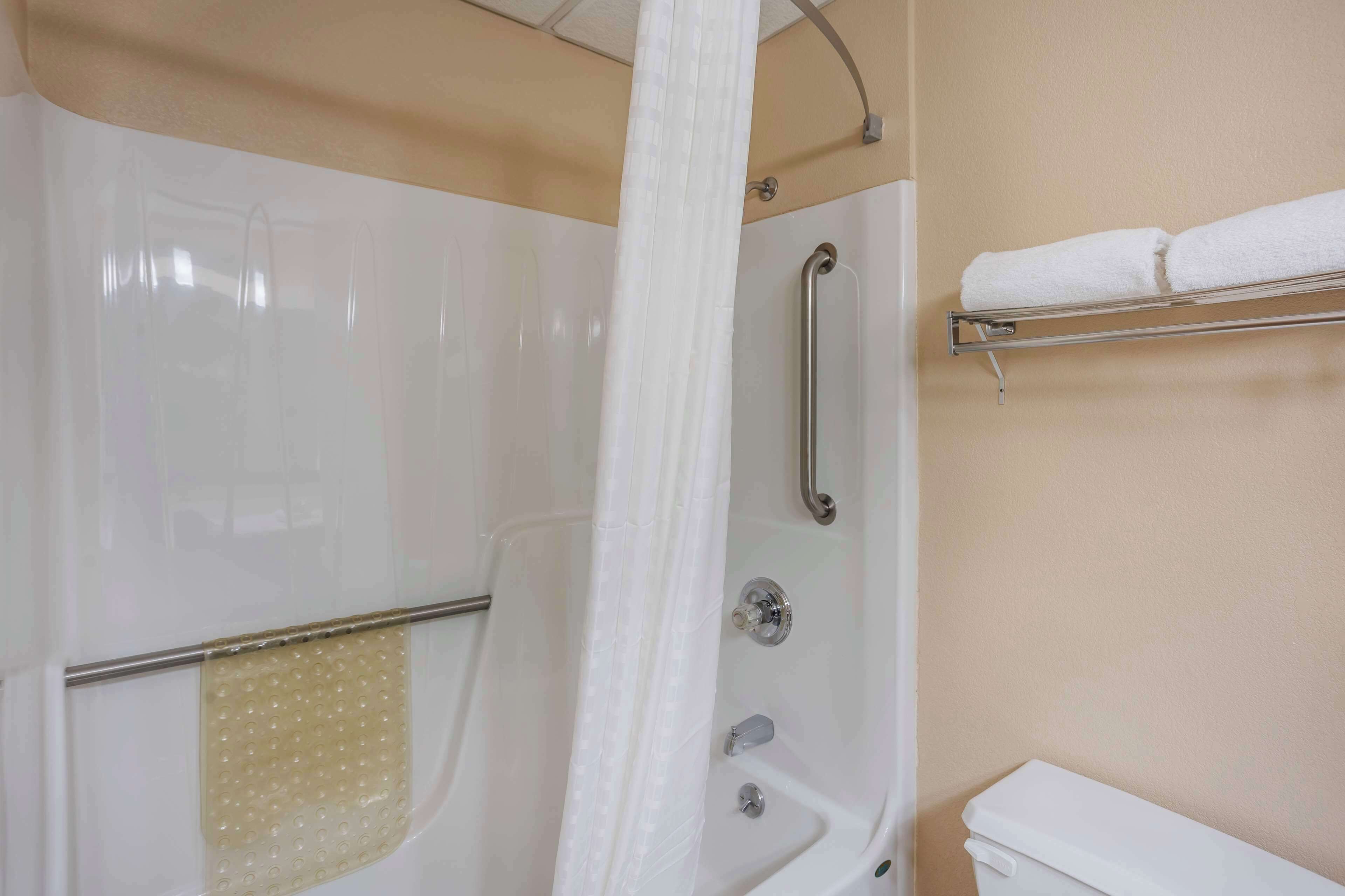 Une salle de bain équipée d’une baignoire, d’une douche avec une barre d’appui, d’un porte-serviettes et de toilettes.