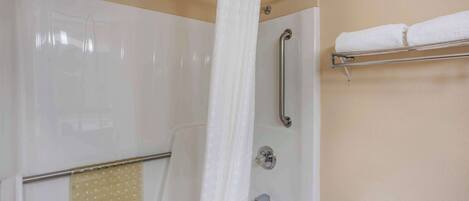 A bathroom with a bathtub, a shower with a handrail, a towel rack, and a toilet.