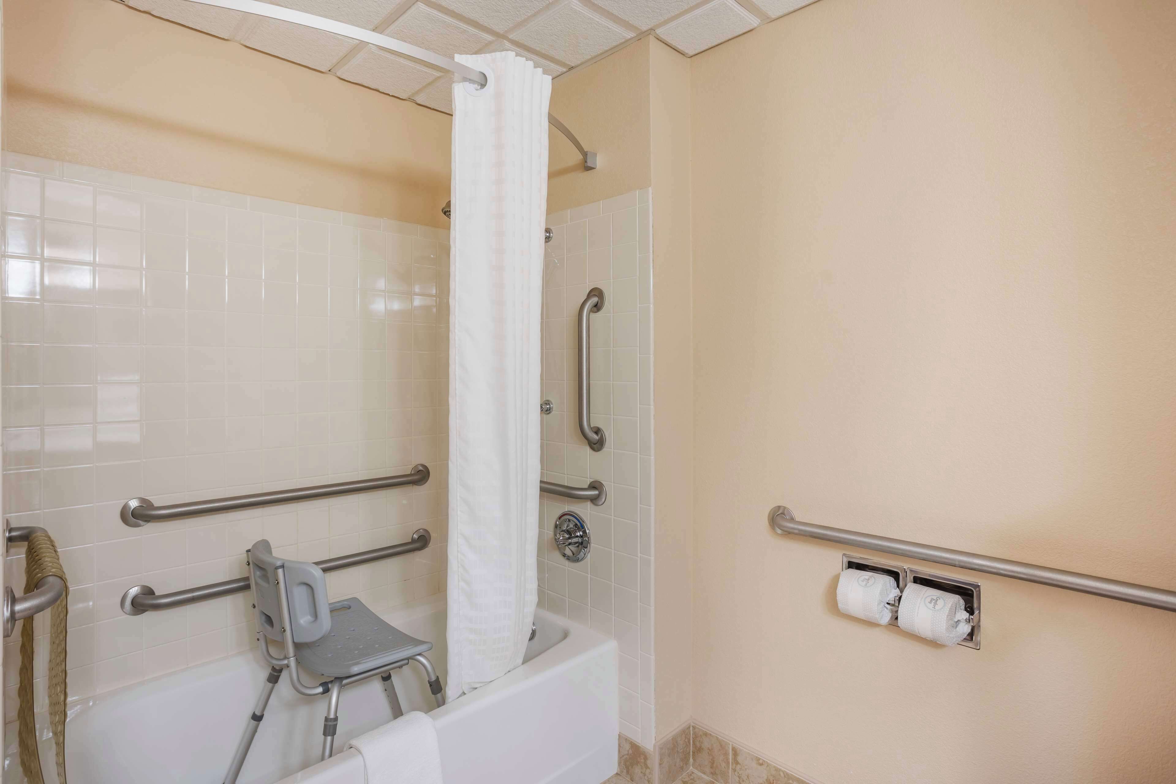 A bathroom with a bathtub, a shower with a grab bar, a wheelchair-accessible bench, and a toilet paper holder.