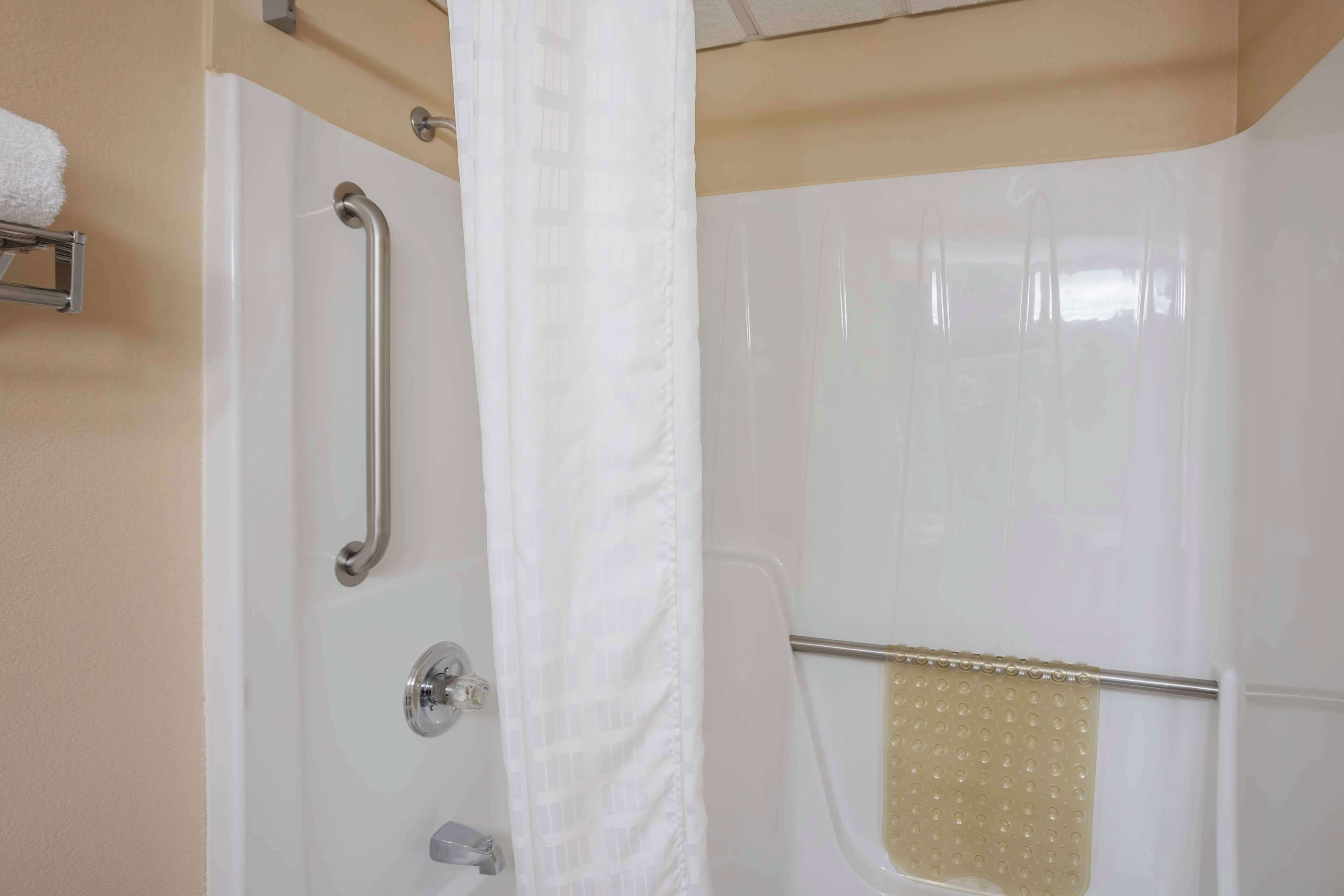 A shower with a grab bar, a towel rack, and a shower curtain.