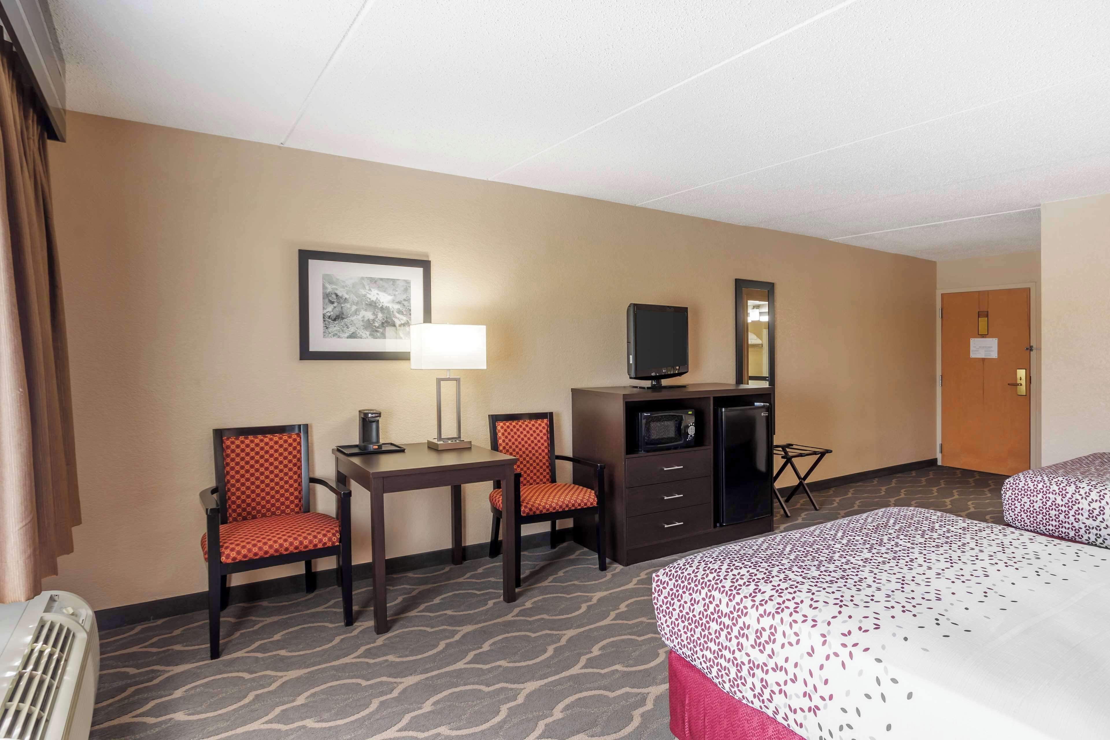 A hotel room with two beds, a desk, two chairs, a television, a microwave, and a heater.