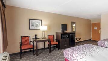 A hotel room with two beds, a desk, two chairs, a television, a microwave, and a heater.