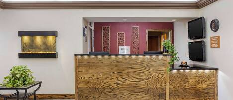 A reception desk with a wooden finish, a wall-mounted television, and a sign indicating the reception area.