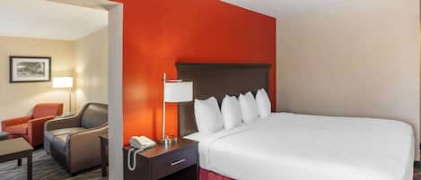 A hotel room with a large bed, a nightstand with a lamp, a chair, and a desk.