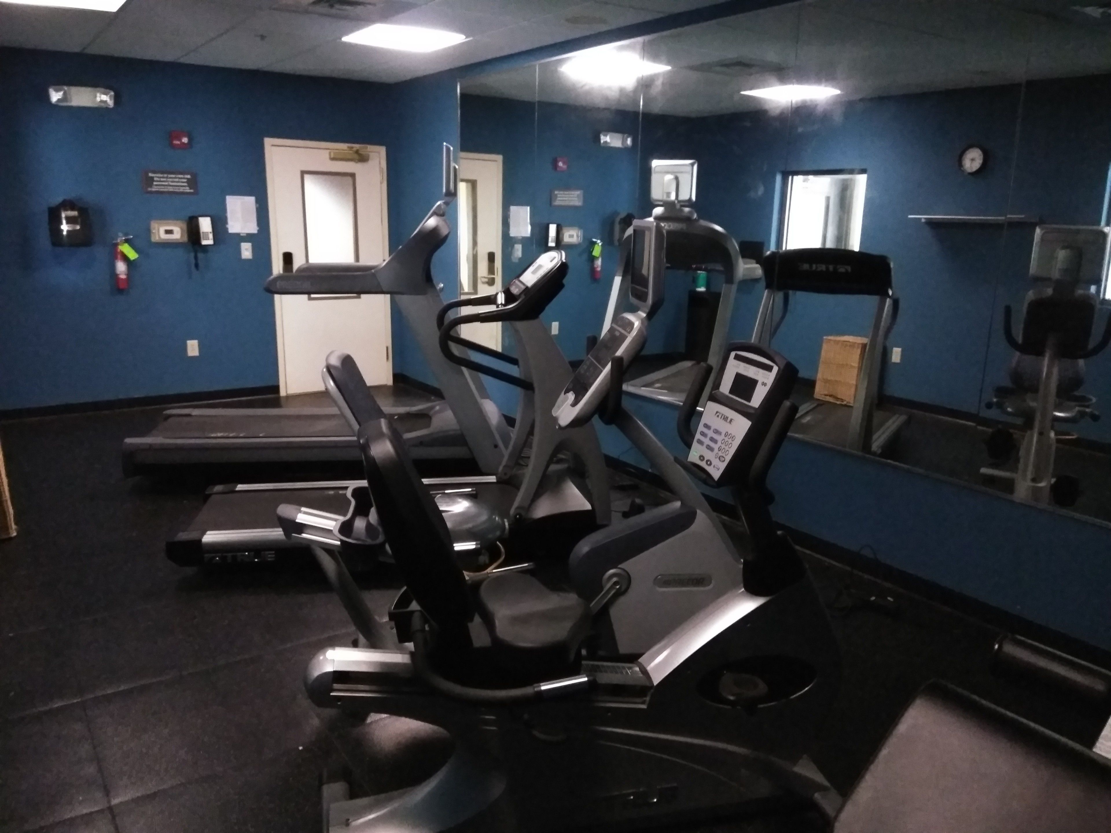 A gym with various exercise equipment, including treadmills and stationary bikes, and a mirrored wall.