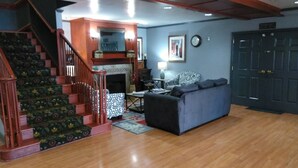 A living room with a staircase, a fireplace, a sofa, and a door. - Baymont by Wyndham Clinton (Clinton)