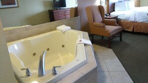 A hotel room with a large bathtub, a chair, a bed, a TV, and a dresser. - Baymont by Wyndham Clinton (Clinton)