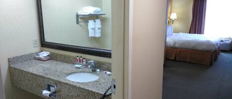 A hotel bathroom with a granite countertop sink, a large mirror, and a towel rack with folded towels.