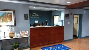 A reception area with a wooden desk, a framed painting, and a sign for Baymont Inn & Suites. - Baymont by Wyndham Clinton (Clinton)
