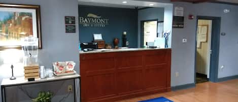 Un área de recepción con un escritorio de madera, un cuadro enmarcado y un cartel de Baymont Inn & Suites.