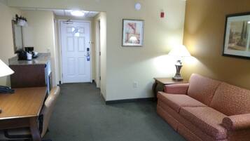 A hotel room with a desk, a sofa, a lamp, and a framed picture on the wall.