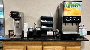 A self-service beverage station with a Bunn coffee machine and a Thirsty machine offering water, orange juice, and apple juice. - Serena Inn & Suites - Sundance (Sundance)