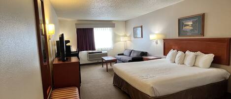 A hotel room with a large bed, a sofa, a desk, and a chair.