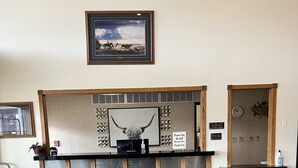 A reception desk with a framed picture above, a clock, and a sign requesting guests to ring the bell for service. - Serena Inn & Suites - Sundance (Sundance)
