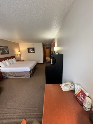 A hotel room with a bed, a desk with a telephone, and a wall-mounted TV.