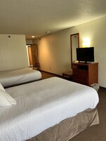 Habitación de hotel con dos camas, un televisor sobre un tocador de madera y un espejo en la pared.