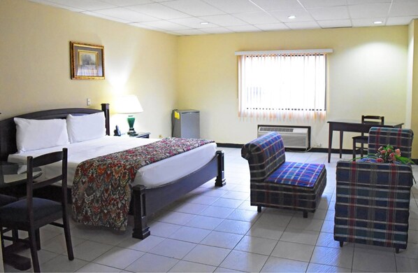 Una habitación de hotel con una cama, una silla, un sofá, una mesa y una ventana con persianas.