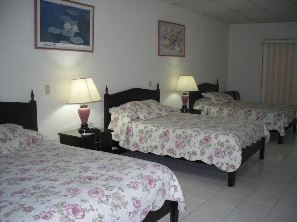 A hotel room with three beds, each with a floral bedspread, bedside lamps, and framed artwork on the walls.