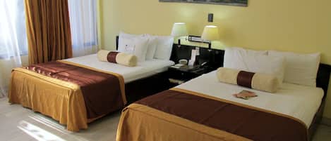 A hotel room with two beds, each with a brown bedspread, white pillows, and a nightstand with a lamp.