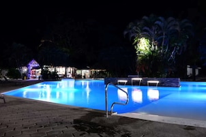 A nighttime swimming pool with illuminated edges and a small waterfall feature.