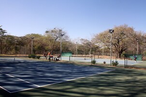 Una cancha de tenis con una red, bancos y árboles al fondo.