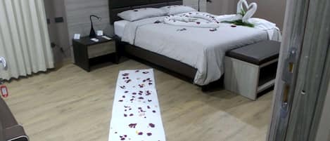A neatly arranged bedroom with a bed, bedside tables, and a long white towel with rose petals on the floor.