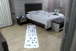 Un dormitorio ordenado con cama, mesitas de noche y una toalla blanca larga con pétalos de rosa en el suelo.