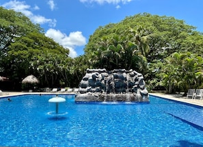 A swimming pool with a rock waterfall feature surrounded by lush greenery. - Best Western El Sitio Hotel (Liberia)