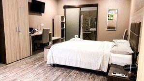 A hotel room with a large bed, a desk, a chair, a wardrobe, a TV, a mirror, and a bathroom with a shower and sink. - Best Western El Sitio Hotel (Liberia)