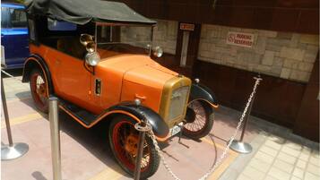 Un coche antiguo exhibido, rodeado por una barrera de cadena, con un cartel de 'PARKING RESERVED' al fondo.