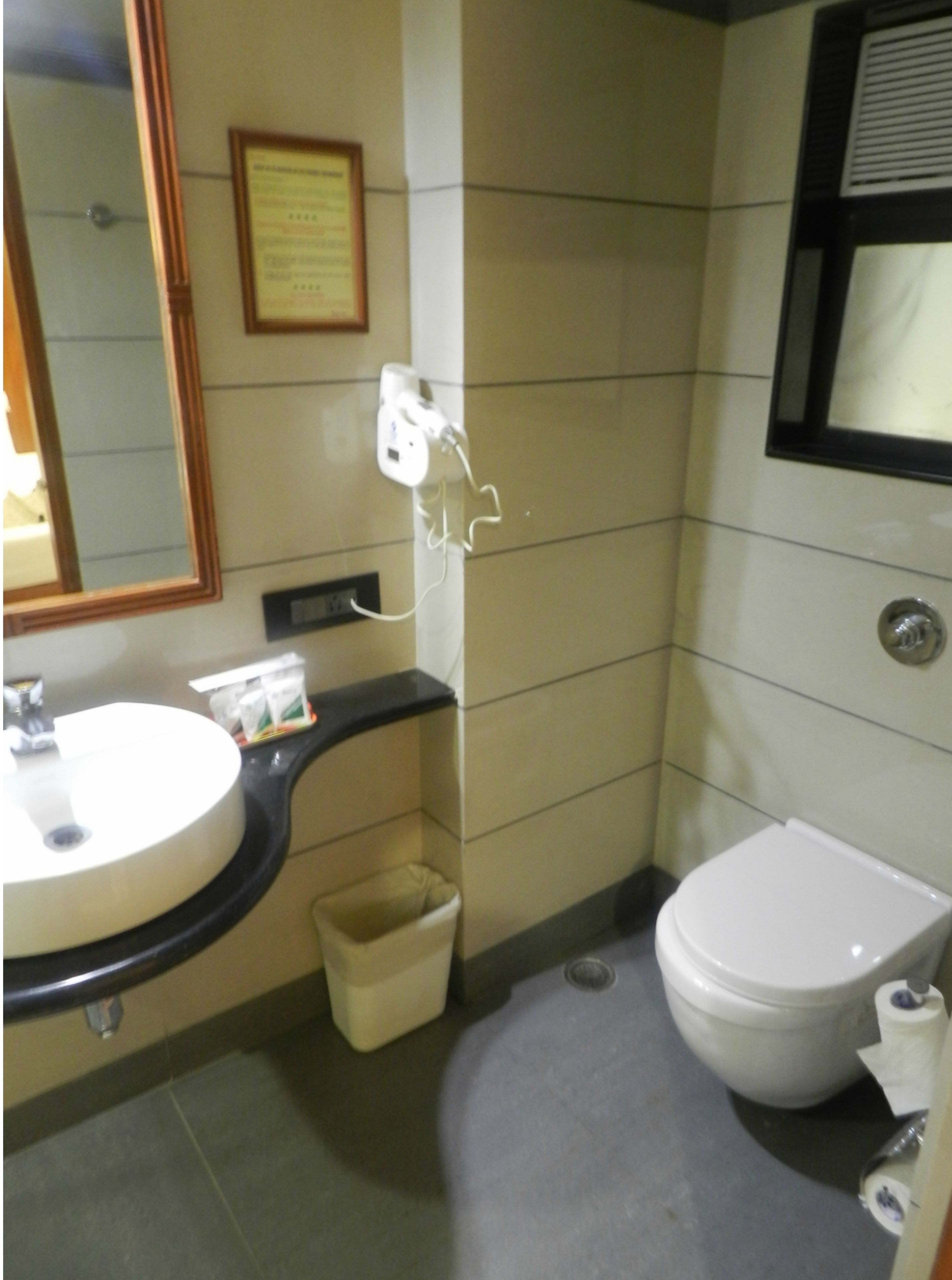 Un baño con lavamanos, espejo, inodoro y cubo de basura.