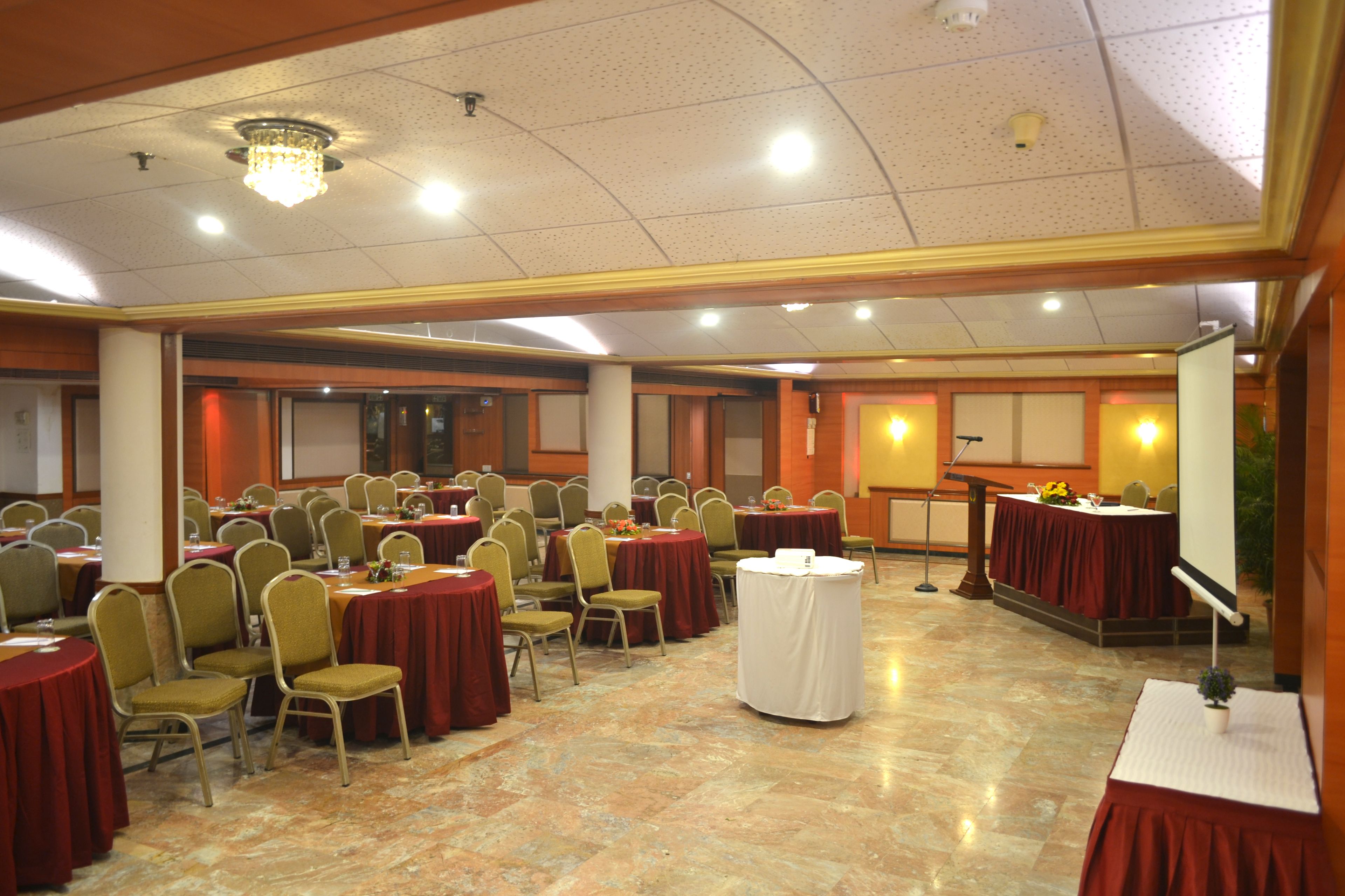 Une salle de banquet avec de nombreuses tables rondes et des chaises, un pupitre et une scène équipée d’un microphone.