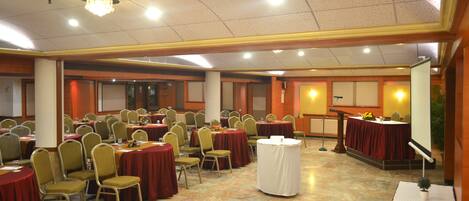 Une salle de banquet avec de nombreuses tables rondes et des chaises, un pupitre et une scène équipée d’un microphone.