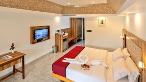 A hotel room with a large bed, a TV, a wooden desk, and a red accent wall. - Swagath Holiday Resort (Neyyattinkara)