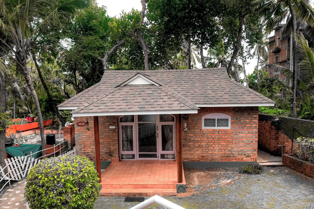 A small brick house with a tiled roof, a front porch, and a visible name sign.