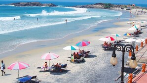 A beach with umbrellas and lounge chairs, a rocky shoreline, and the ocean. - Swagath Holiday Resort (Neyyattinkara)