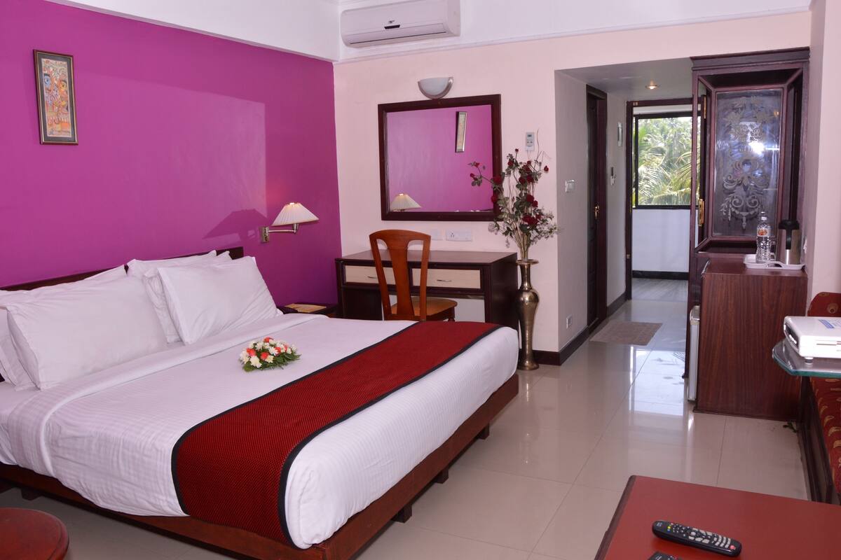 A hotel room with a bed, a desk, a chair, a mirror, and a view of the outside.