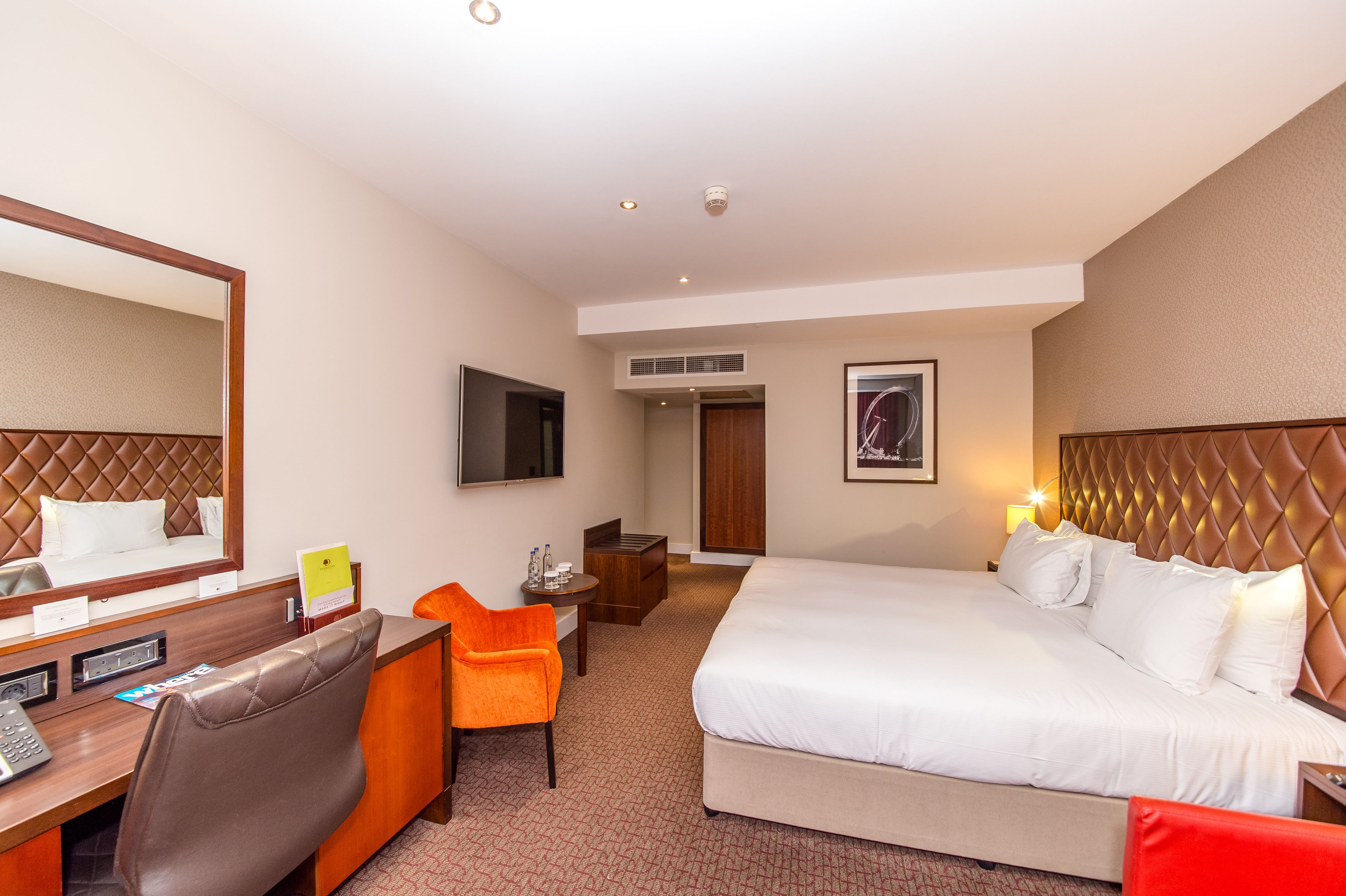 A hotel room with a large bed, a desk with a chair, a television, and a small table with a chair.
