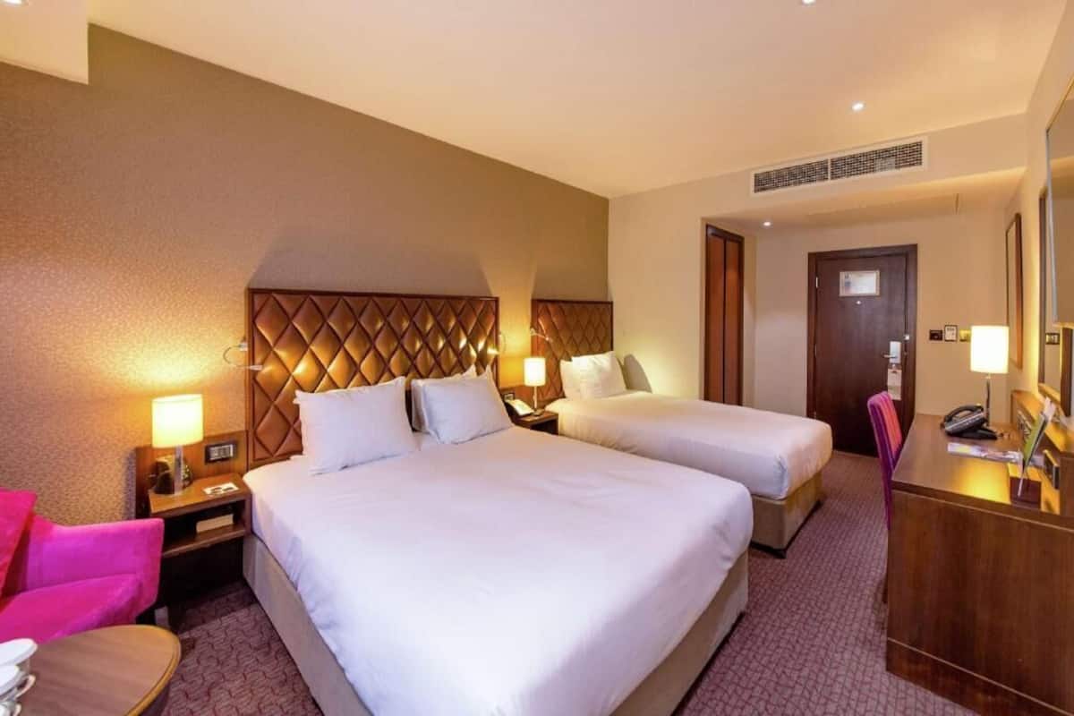 A hotel room with two beds, a desk, a chair, and a mirror.