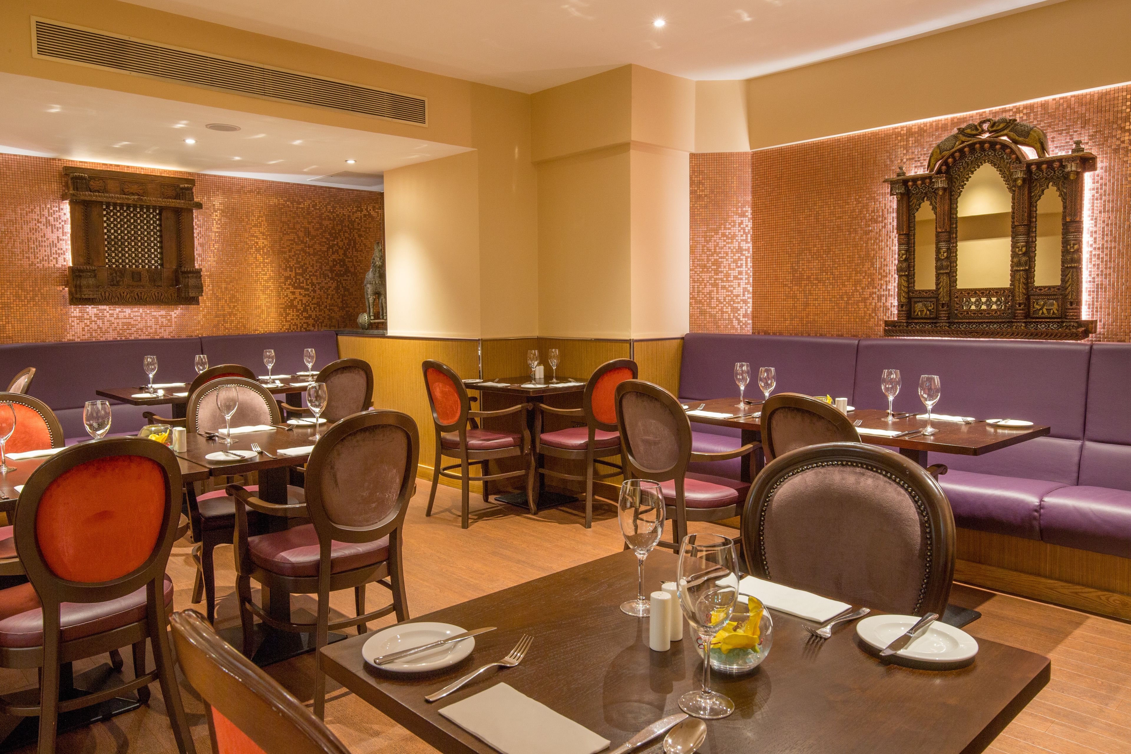 A restaurant with multiple dining tables and chairs, a cushioned booth, and a decorative mirror on the wall.