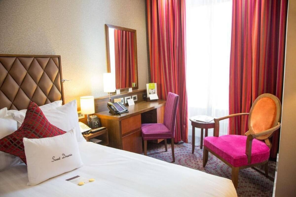 A hotel room with a bed, a desk, a chair, a telephone, and a mirror.