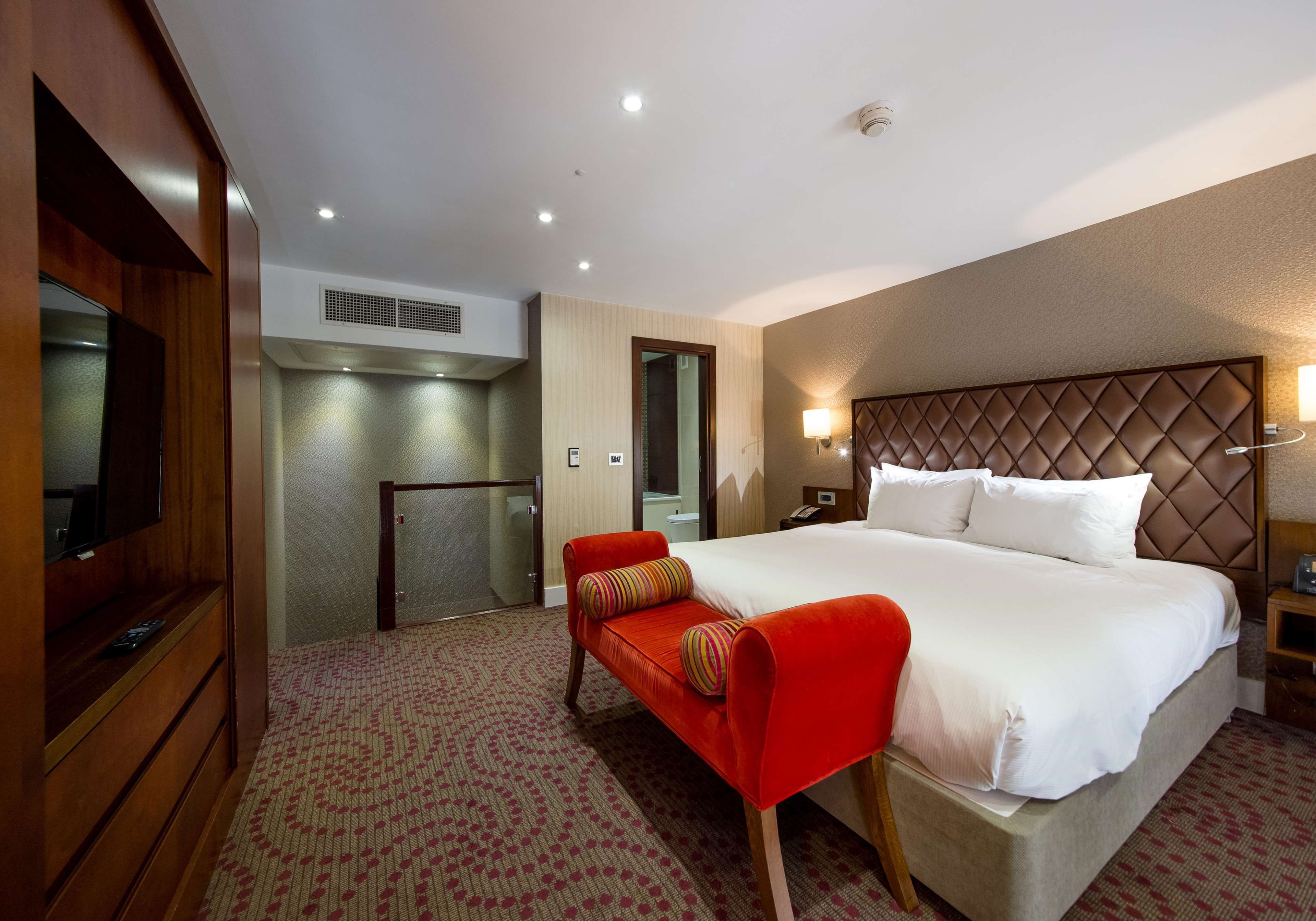 A hotel room with a bed, a TV, a desk, and a chair.