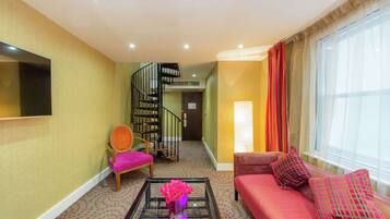 A living room with a sofa, a chair, a coffee table with a vase, a staircase, and a TV mounted on the wall.