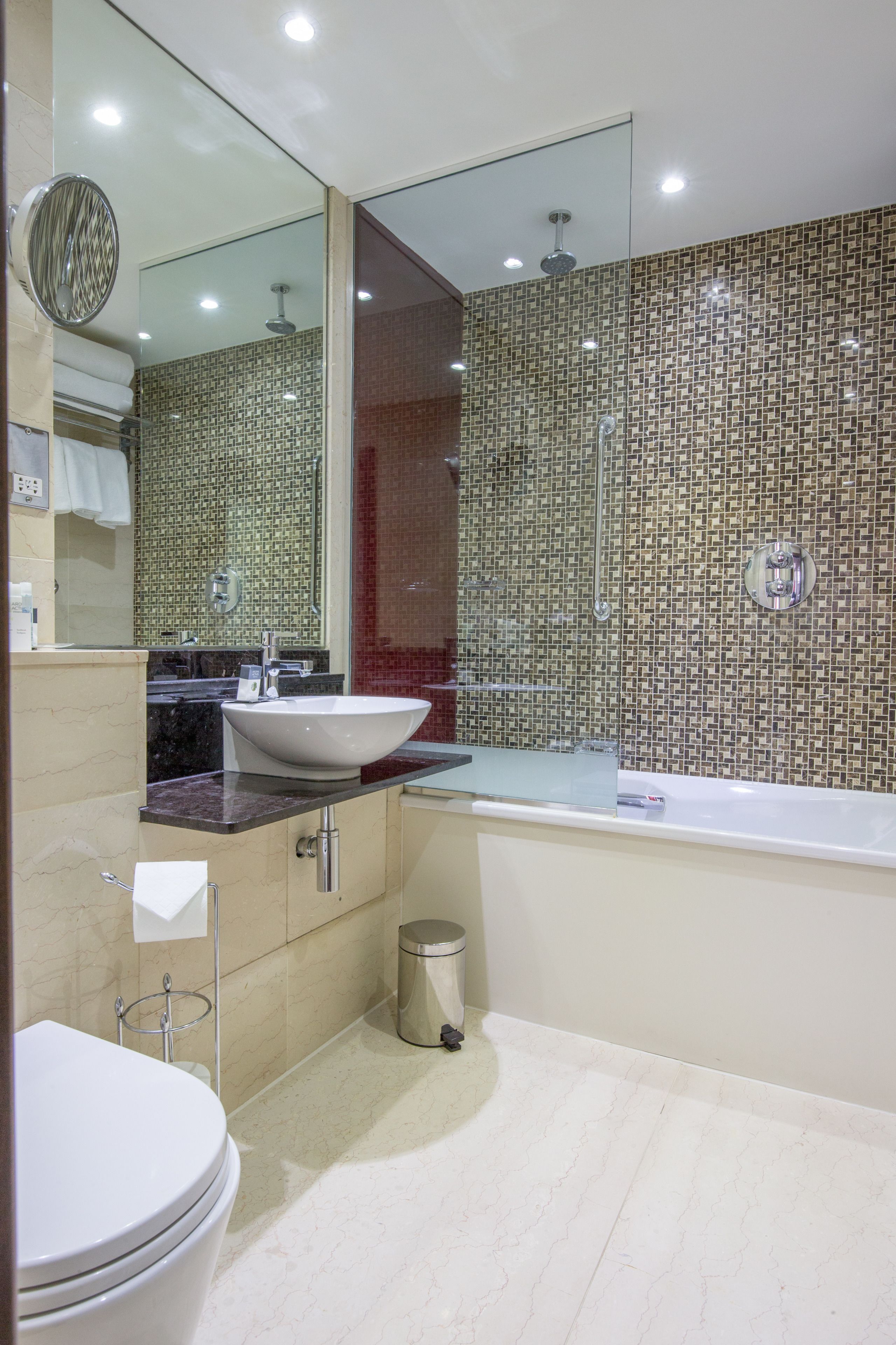 A modern bathroom with a white sink, a large mirror, a bathtub, and a tiled shower wall.