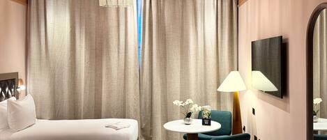 Una habitación de hotel con una cama, una mesa redonda con una silla, una lámpara y un televisor fijado a la pared.